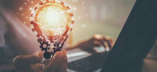 a person holding a light bulb whilst typing on a keyboard