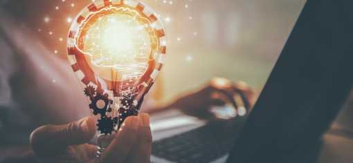 a person holding a light bulb whilst typing on a keyboard